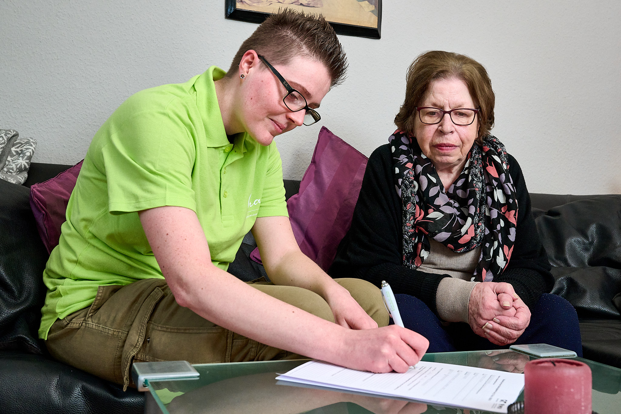 Eine Mitarbeiterin links protokolliert etwas, das die ältere Dame rechts ihr mitteilt.